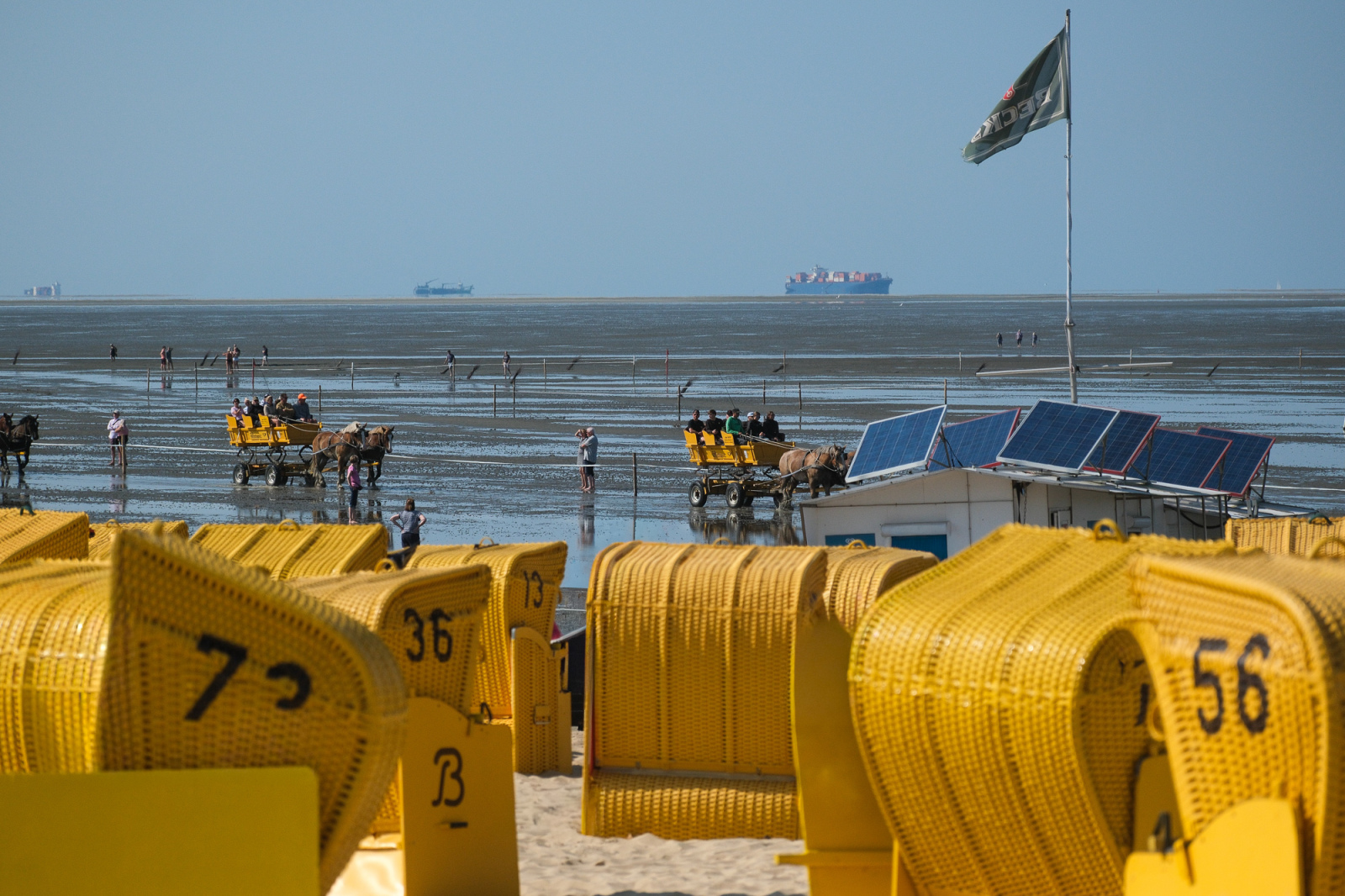 Von gemieteten Strandkörben geht der Blick in die Weite. Im Hintergrund große Frachtschiffe mit dem Ziel Hamburg