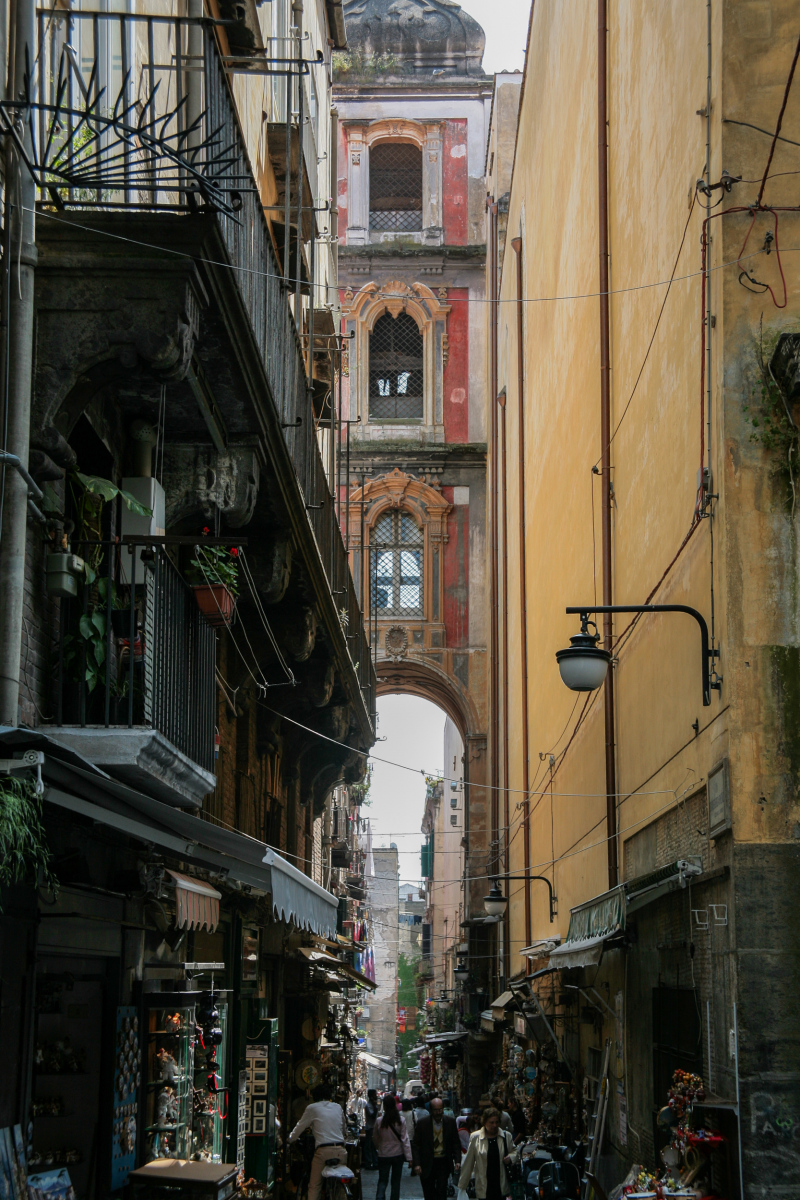 Die belebte Gasse mit dem markanten Glockenturm im Hintergrund ist die Via San Gregorio Armeno. Die Straße liegt im historischen Zentrum und ist weltberühmt für ihre ganzjährig geöffneten Werkstätten zur Herstellung von Weihnachtskrippen, den sogenannten presepi. Zur Via San Gregorio Armeno. Die Straße folgt dem Verlauf eines der antiken römischen cardini (Nord-Süd-Straßen), die das schachbrettartige Stadtbild des alten Neapels prägten. Sie verbindet die beiden Hauptverkehrsadern Via dei Tribunali und Via San Biagio dei Librai.