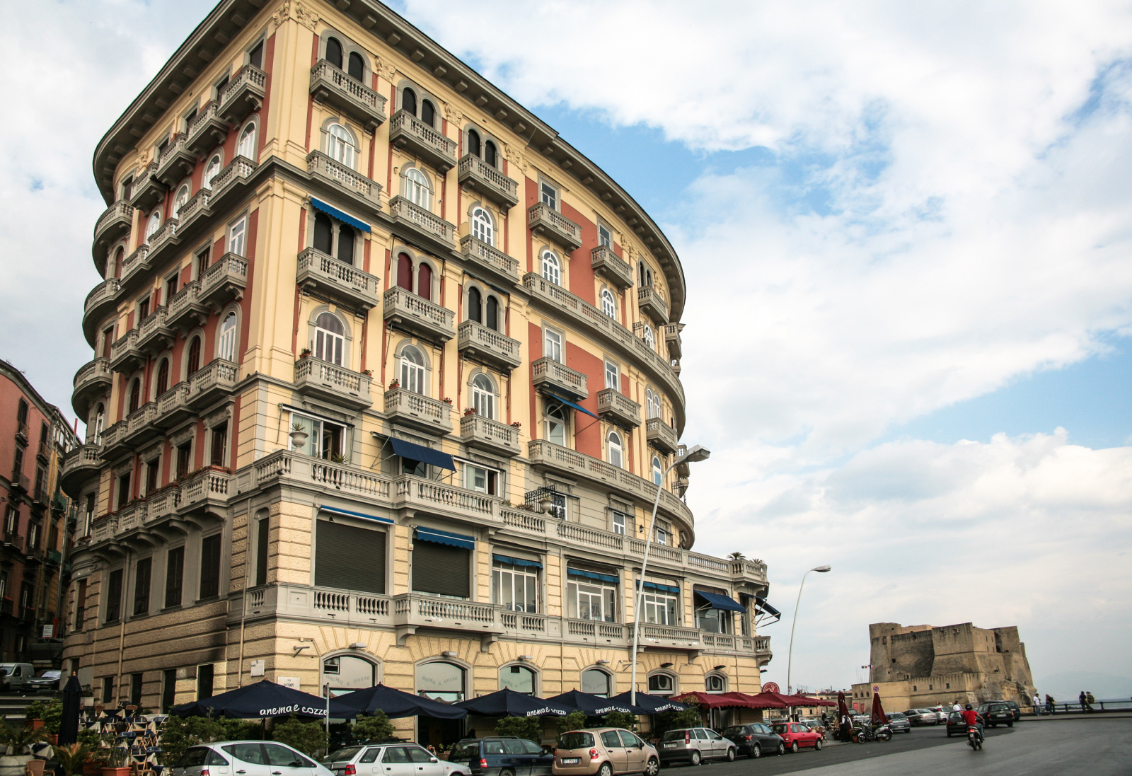 Das Gebäude befindet sich an der Via Partenope und ist als Palazzo Cosenza 57 bekannt. Im Hintergrund außerdem das Castel dell'Ovo, die älteste erhaltene Festung der Stadt. Die Via Partenope ist eine bekannte Uferpromenade am Golf von Neapel, die für ihre malerische Aussicht und zahlreiche Restaurants, Bars und Hotels bekannt ist. Der Palazzo Cosenza 57 wurde zwischen 1918 und 1924 nach Plänen des Architekten Giovanni De Fazio erbaut