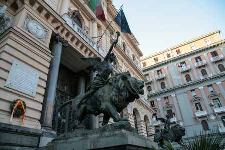 Eine der Bronzestatuen am Eingang des Palazzo della Borsa. Das Gebäude befindet sich an der Piazza Giovanni Bovio. Die Statuen zeigen geflügelte Genien (Putten), die auf Löwen reiten. Sie stellen allegorisch die Macht des Geistes dar, die die wilde, natürliche Kraft dominiert und kontrolliert.