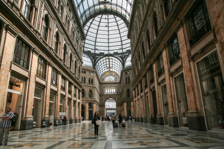 Galleria Umberto I, eine bekannte, überdachte Einkaufsgalerie in Neapel, Italien. Standort: Die Galerie befindet sich im Herzen von Neapel, direkt gegenüber dem berühmten Opernhaus Teatro San Carlo.Architektur: Sie wurde in den Jahren 1887 bis 1890 erbaut und ist für ihre imposante Glas- und Eisenkuppel sowie die eleganten Marmorböden mit Mosaikmustern bekannt. Die Haupteingänge sind durch elegante Bögen und beeindruckende Verzierungen gekennzeichnet.Atmosphäre: Die Galerie ist ein beliebter Treffpunkt und beherbergt Geschäfte, Cafés und Büros. Da es sich um einen öffentlich zugänglichen Raum handelt, ist der Eintritt frei.