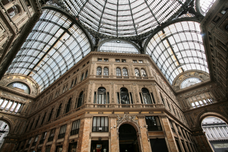 Der abgebildete Ort ist die Galleria Umberto I, eine bekannte, überdachte Einkaufsgalerie in Neapel, Italien. Standort: Die Galerie befindet sich im Herzen von Neapel, direkt gegenüber dem berühmten Opernhaus Teatro San Carlo.Architektur: Sie wurde in den Jahren 1887 bis 1890 erbaut und ist für ihre imposante Glas- und Eisenkuppel sowie die eleganten Marmorböden mit Mosaikmustern bekannt. Die Haupteingänge sind durch elegante Bögen und beeindruckende Verzierungen gekennzeichnet.Atmosphäre: Die Galerie ist ein beliebter Treffpunkt und beherbergt Geschäfte, Cafés und Büros. Da es sich um einen öffentlich zugänglichen Raum handelt, ist der Eintritt frei.