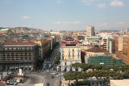 Corso Umberto I (auch Rettifilo genannt), eine wichtige Verkehrsader im Zentrum von Neapel, Italien. Standort: Die Straße erstreckt sich vom Hauptbahnhof (Piazza Garibaldi) bis zur Piazza Bovio und ist eine der Hauptachsen des historischen Zentrums.Architektur: Die Gebäude entlang des Corso Umberto I wurden im Zuge einer umfassenden Stadtsanierung im späten 19. Jahrhundert im neoklassizistischen Stil erbaut.Der Platz: An der Kreuzung mit der Via Duomo (erkennbar an der prominenten Straßenführung) befindet sich die Piazza Nicola Amore, die die auch als "Platz der vier Palazzi" bekannt ist. Die hohen Gebäude mit den charakteristischen Statuen sind typisch für diesen Platz.