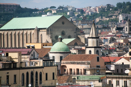 Das große Gebäude mit dem markanten grünen Dach ist die Basilika Santa Chiara (Complesso Monumentale di Santa Chiara) in Neapel, Italien.Standort: Die Basilika befindet sich im Herzen der Altstadt von Neapel, in der Nähe der Spaccanapoli, einer der Hauptstraßen der Stadt.Architektur: Die Kirche ist ein bedeutendes Beispiel der gotischen Architektur in Neapel. Das Gebäude im Vordergrund mit der kleineren grünen Kuppel ist ebenfalls Teil des monumentalen Komplexes.Geschichte: Die Kirche wurde im 14. Jahrhundert erbaut, aber im Zweiten Weltkrieg schwer beschädigt und anschließend in ihrem ursprüngliche