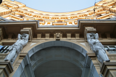 Das Gebäude auf dem Bild befindet sich an der Piazza Nicola Amore 14 in Neapel, Italien.Architektur: Das Gebäude zeichnet sich durch seine halbkreisförmige Fassade mit markanten Statuen, sogenannten Telamonen, aus, die die Last des oberen Stockwerks zu tragen scheinen. Diese architektonischen Details sind typisch für das Design des Gebäudes.Standort: Die Piazza Nicola Amore ist ein Platz im historischen Zentrum, in der Nähe des Corso Umberto I und der Via Duomo.